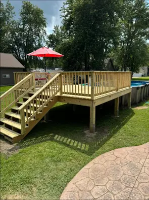 New wood pool deck with stairs and railing beside an above-ground pool