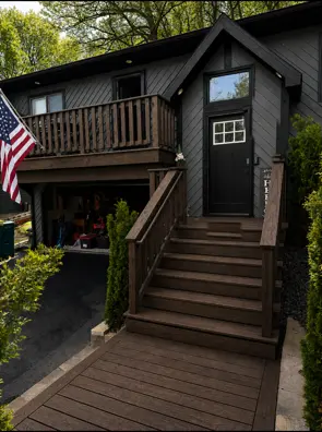 Dark wood-tone front stairs and balcony deck on a black-sided home
