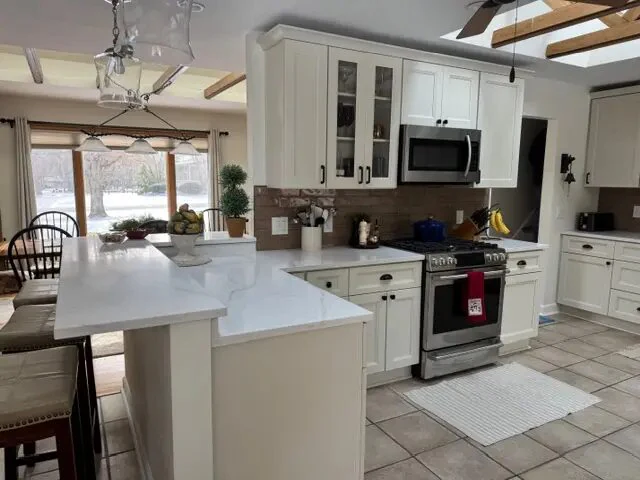 Completed white kitchen with peninsula seating, glass-front cabinets, and exposed ceiling beams